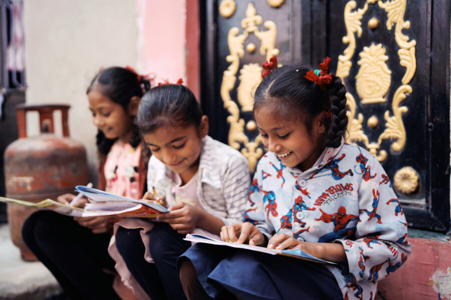 Three young girls reading picture books at a Pratham Mohalla Library.